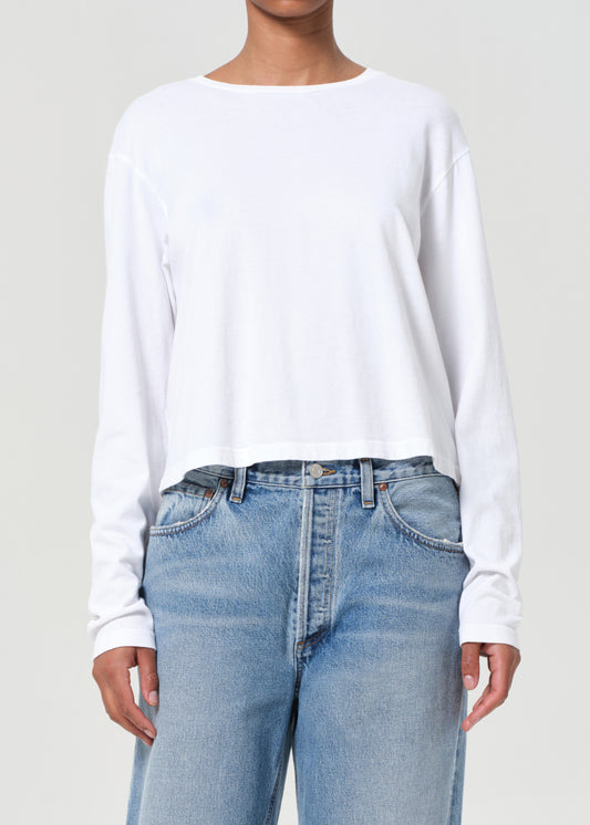 Person wearing a white long-sleeve shirt and light blue jeans on a plain background