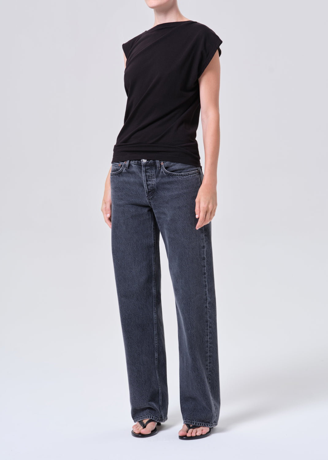 Person wearing a black sleeveless top and blue jeans on a white background