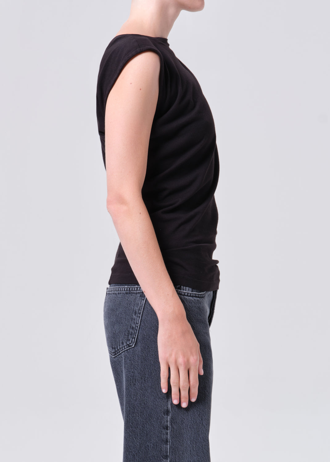 Person wearing a black sleeveless top and blue jeans on a light gray background