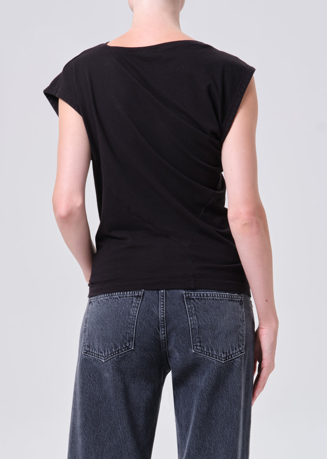 Person wearing a black sleeveless top and blue jeans on a plain background