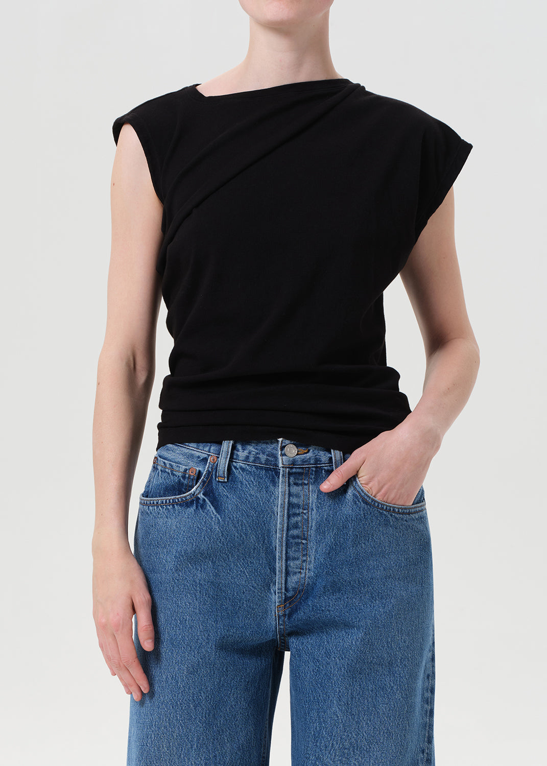 Person wearing a black sleeveless top and blue jeans on a light gray background