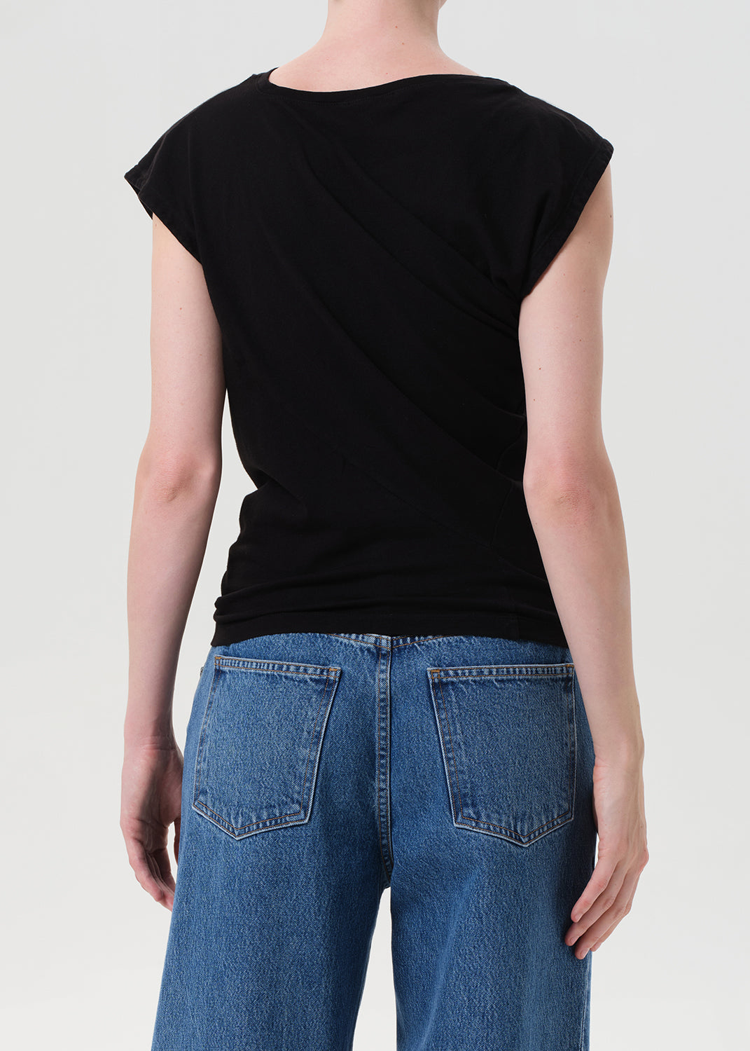 Person wearing a black top and blue jeans on a plain background