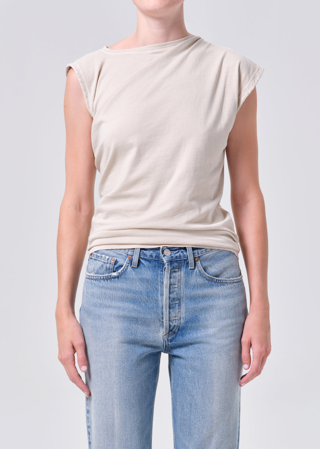 Person wearing a beige sleeveless top and light blue jeans on a plain background