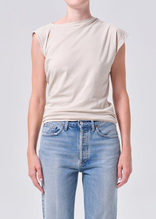 Person wearing a beige sleeveless top and light blue jeans on a plain background