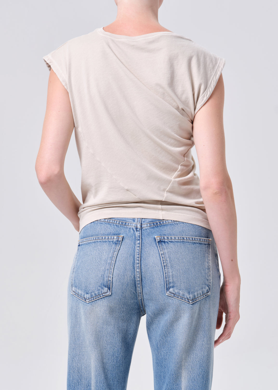Person wearing a beige sleeveless top and light blue jeans on a plain background