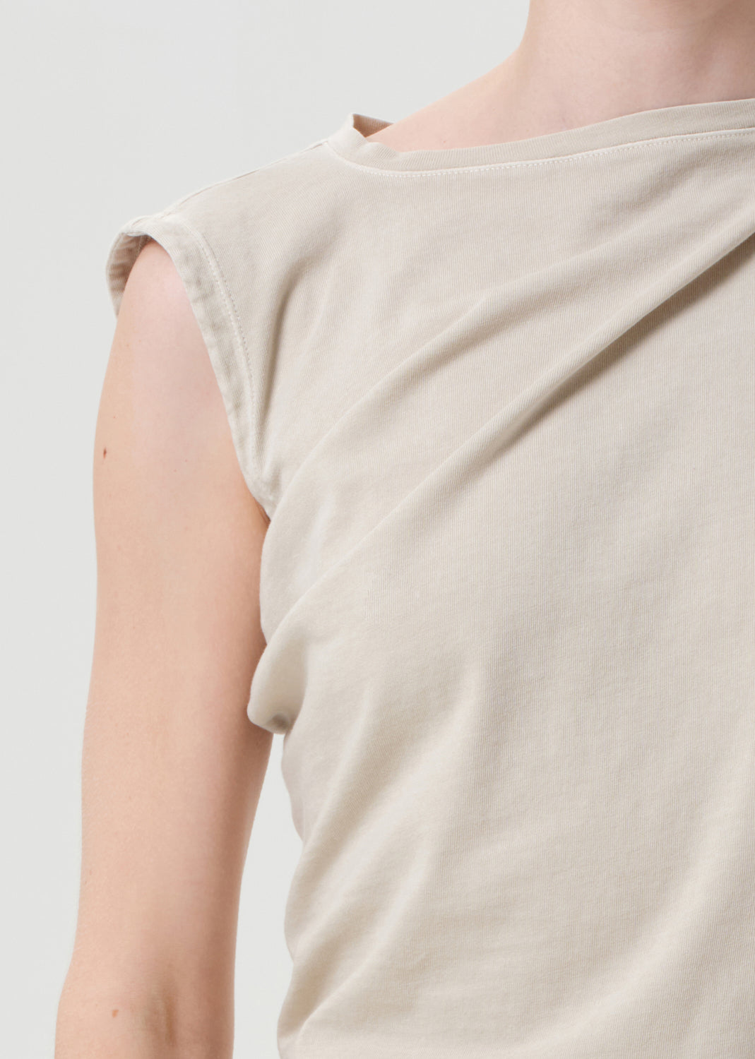 Close-up of a person wearing a beige sleeveless top against a light gray background