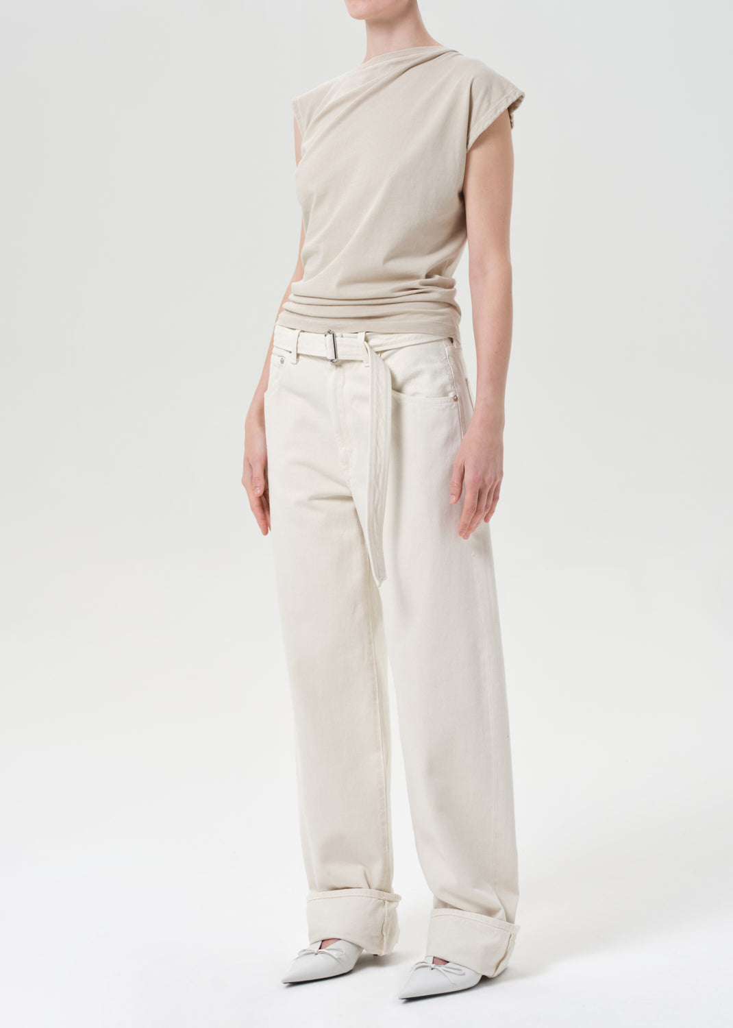 Person wearing a beige sleeveless top and light-colored pants on a white background