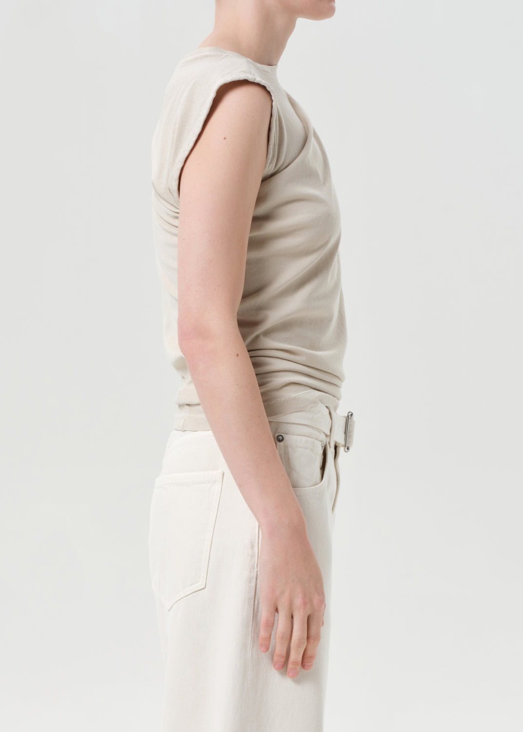 Person wearing a beige sleeveless top and white pants on a light background