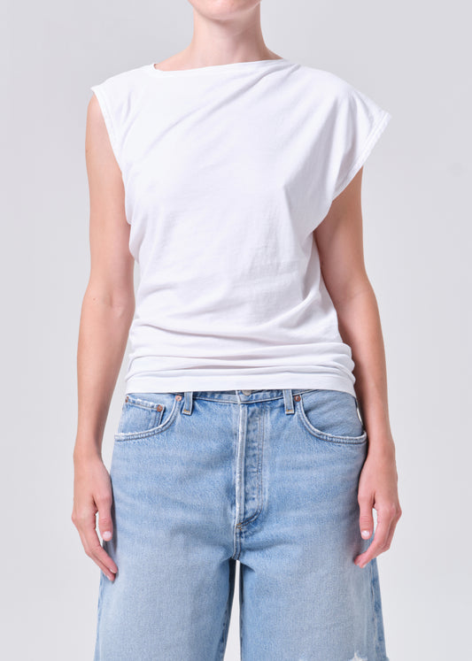 Person wearing a white sleeveless top and light blue jeans on a plain background