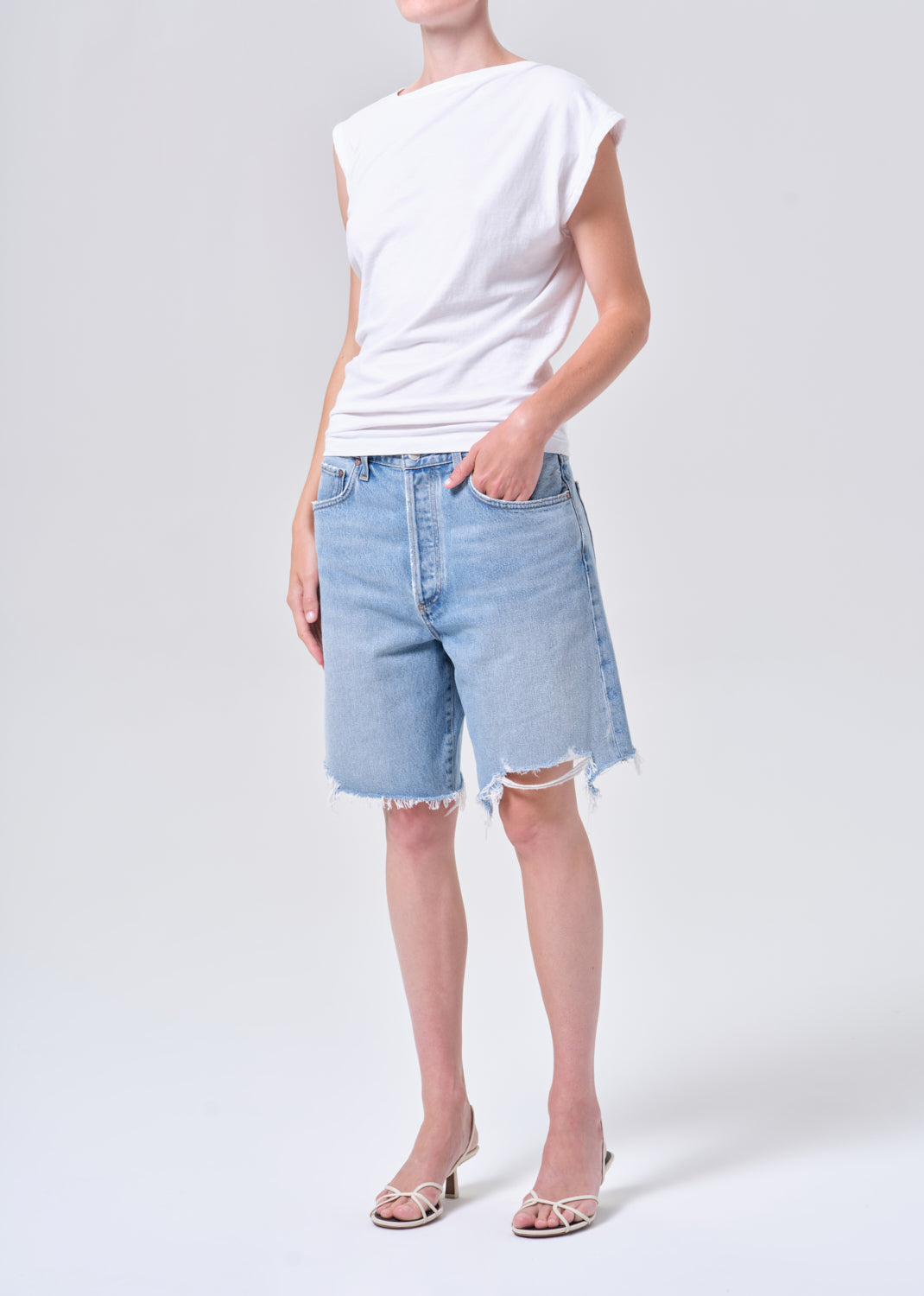 Person wearing a white sleeveless top and light blue denim shorts on a white background