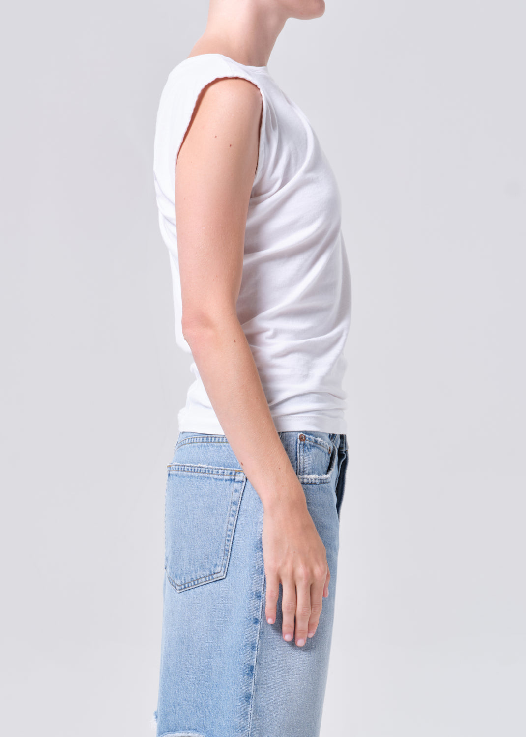Person wearing a white sleeveless top and light blue jeans on a plain background