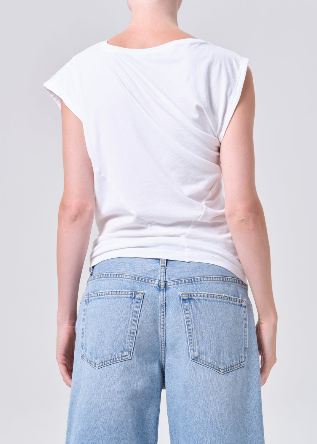Person wearing a white sleeveless top and light blue jeans on a plain background