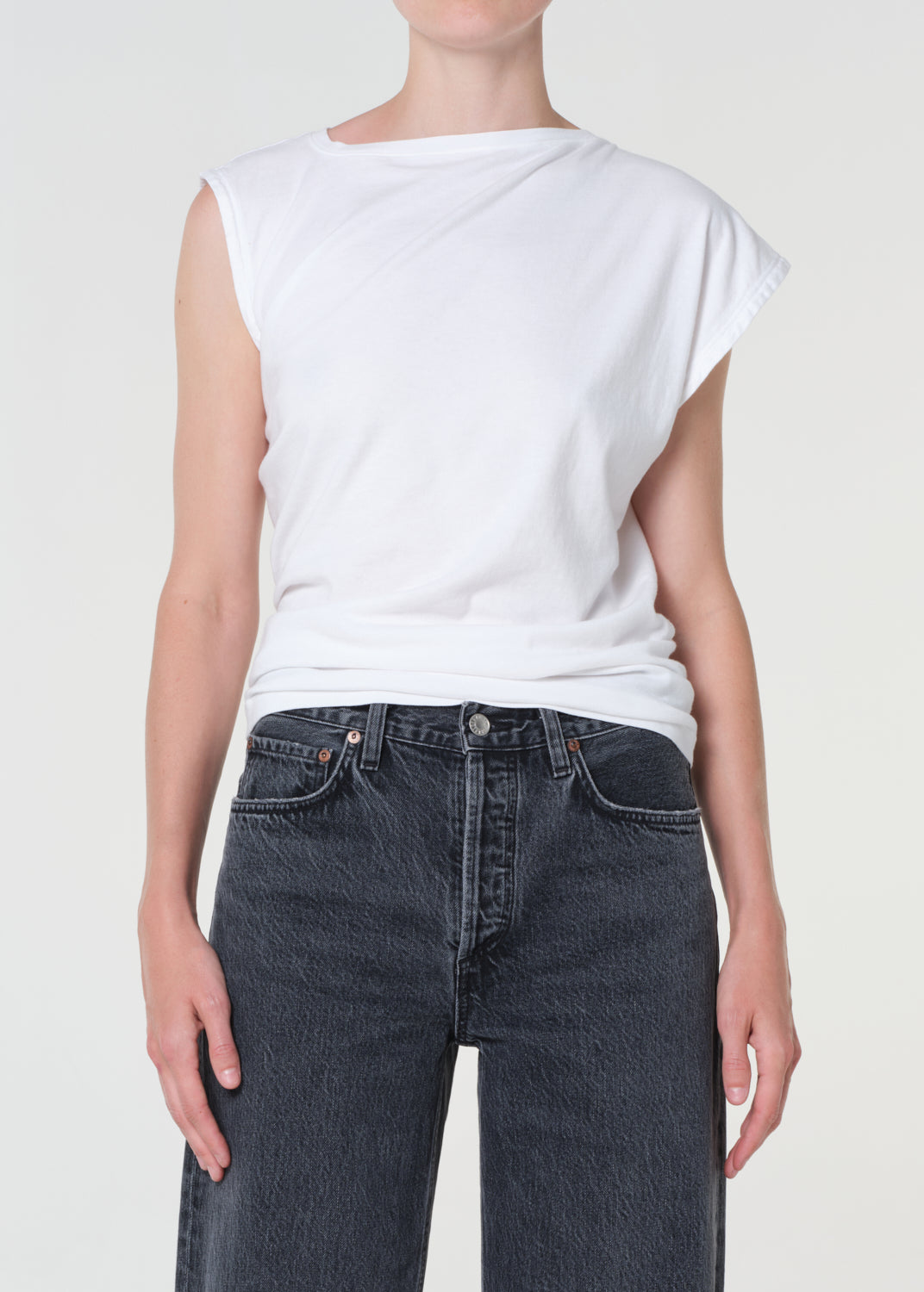 Person wearing a white sleeveless top and dark jeans on a plain background