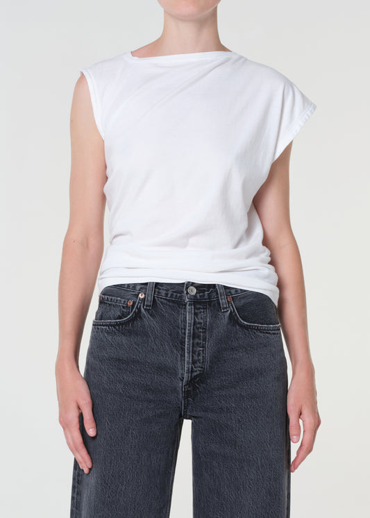 Person wearing a white sleeveless top and dark jeans on a plain background