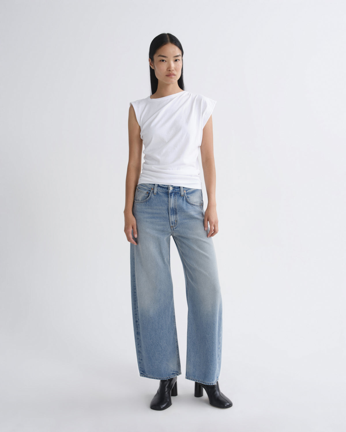 Person wearing a white top and light blue jeans on a plain background