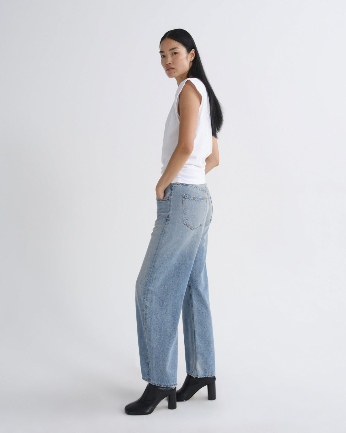 Person wearing a white top and light blue jeans on a plain background