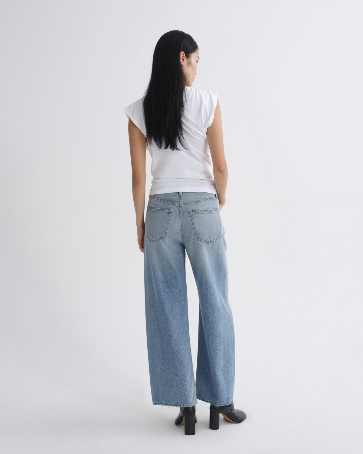 Person wearing a white top and light blue jeans on a plain background
