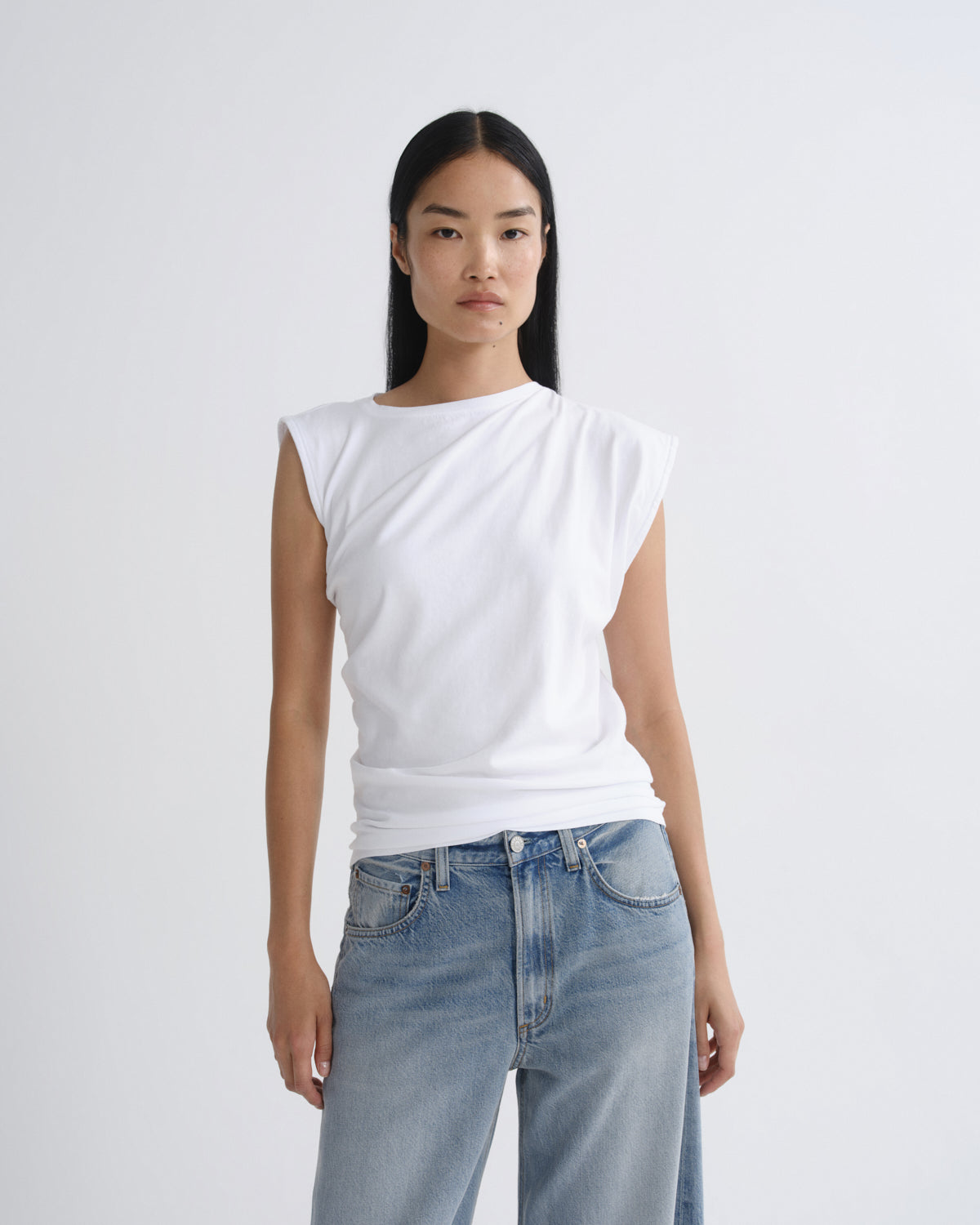 Person wearing a white top and light blue jeans on a plain background