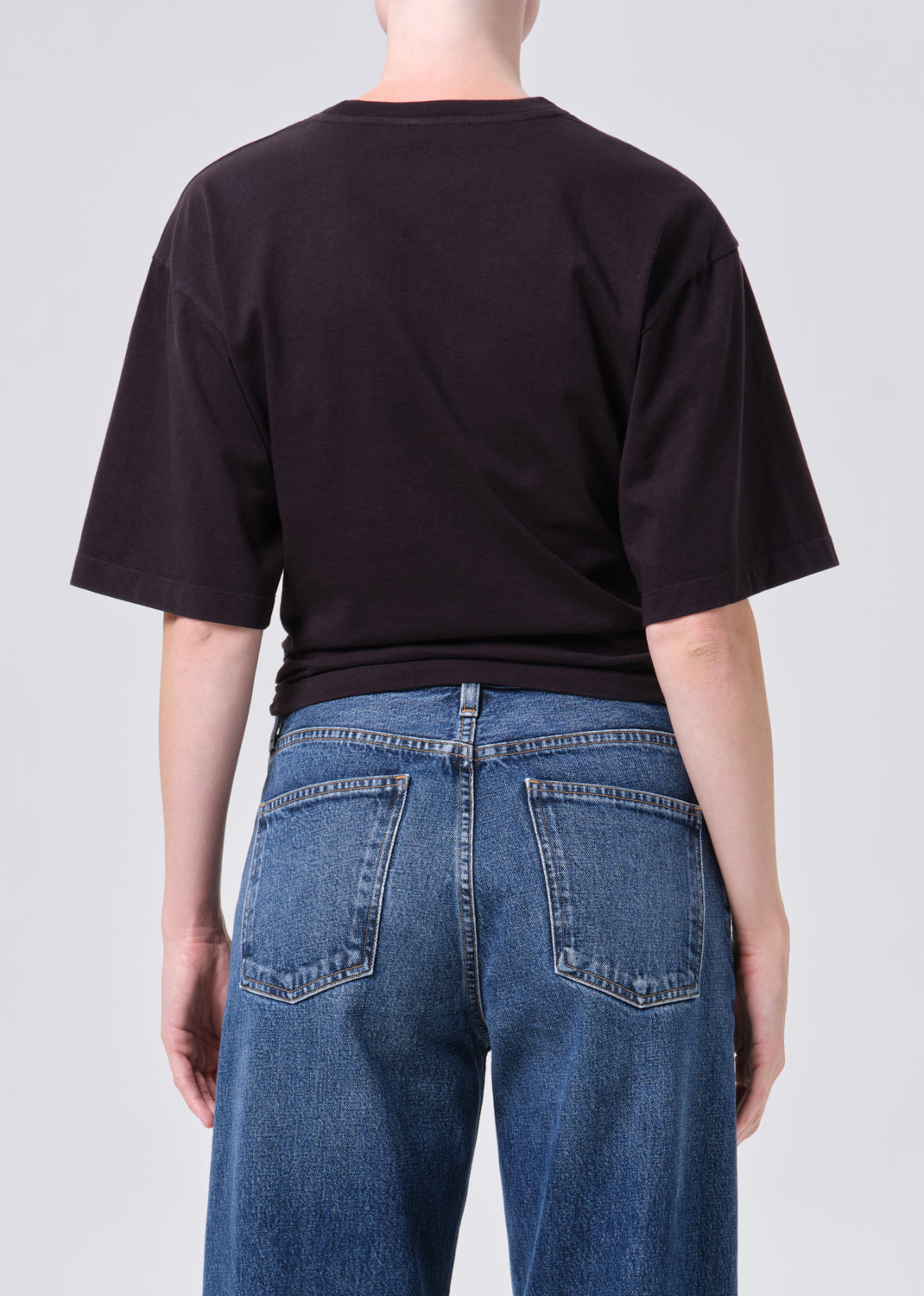 Person wearing a black t-shirt and blue jeans on a plain background