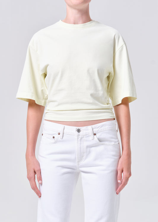 Person wearing a light yellow cropped t-shirt and white jeans on a plain background