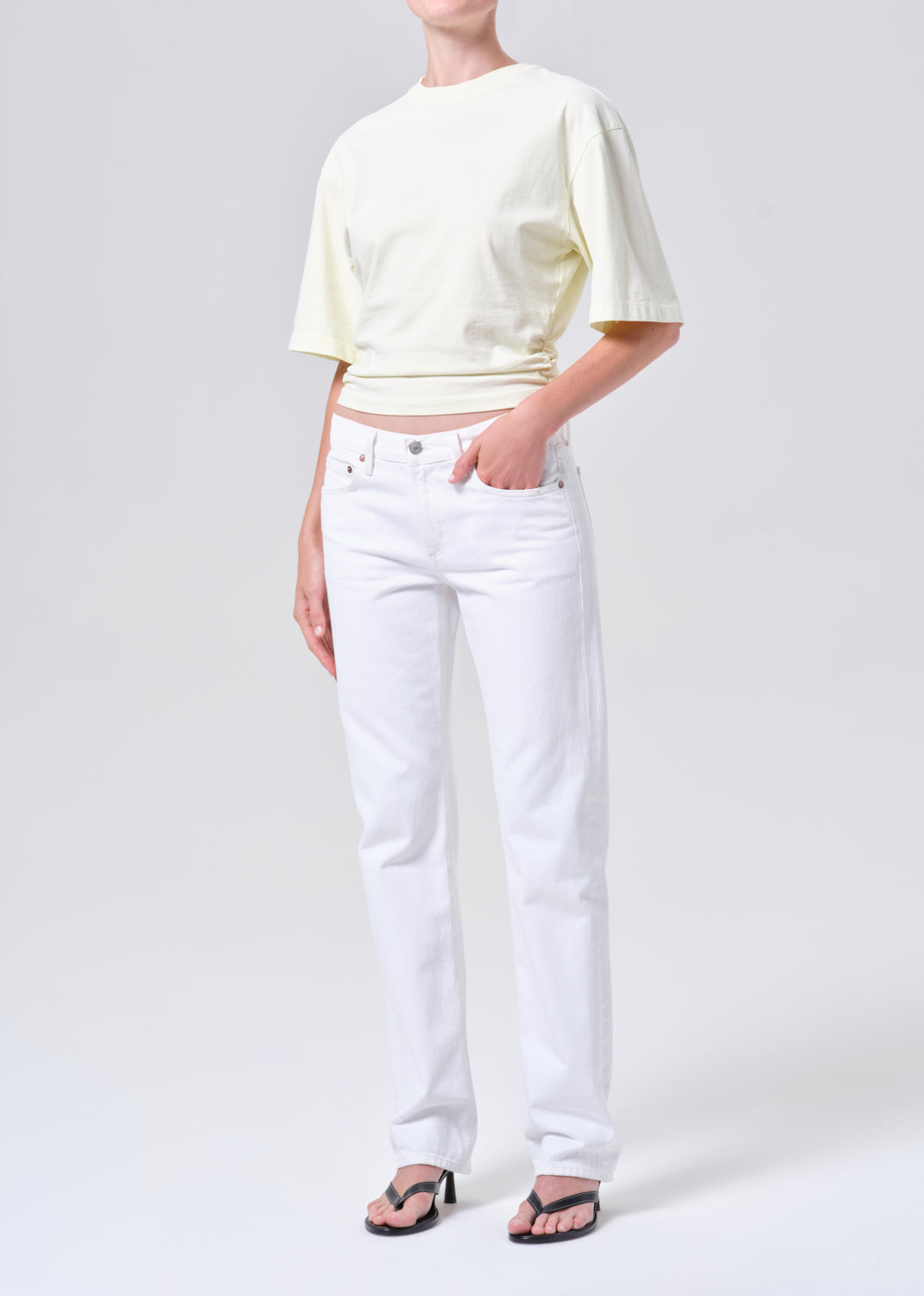 Person wearing a light yellow crop top and white jeans on a plain background