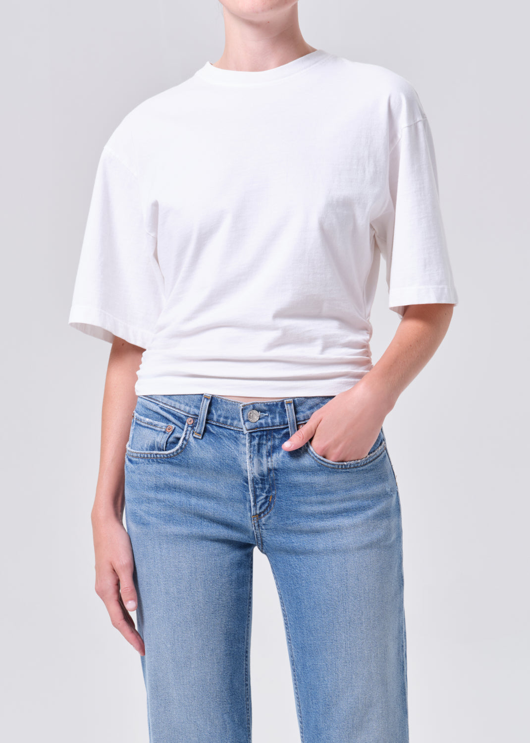 Person wearing a white t-shirt and light blue jeans on a plain background