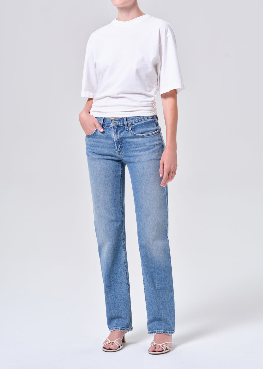 Person wearing a white t-shirt and light blue jeans on a plain background