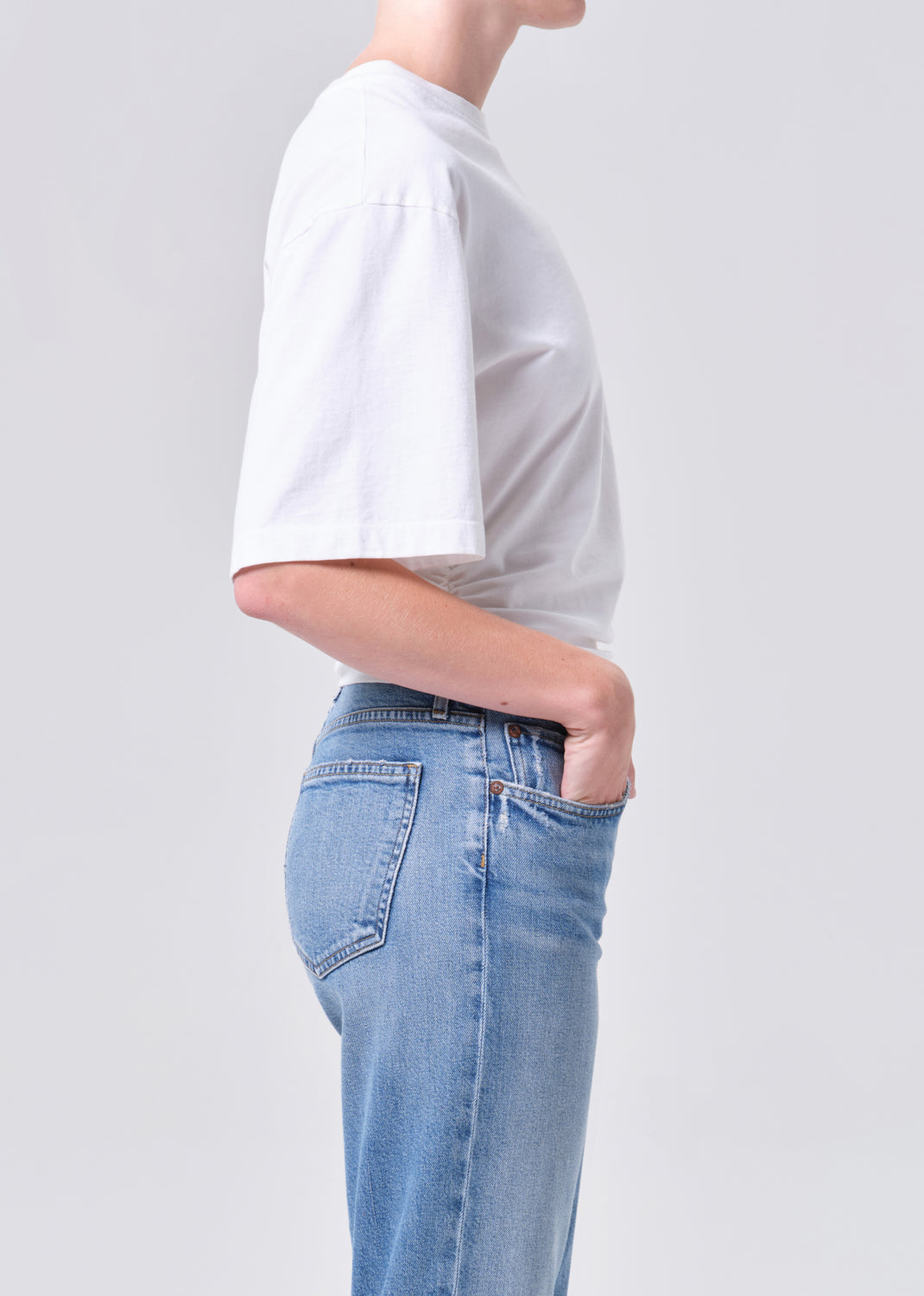 Person wearing a white t-shirt and light blue jeans on a plain background