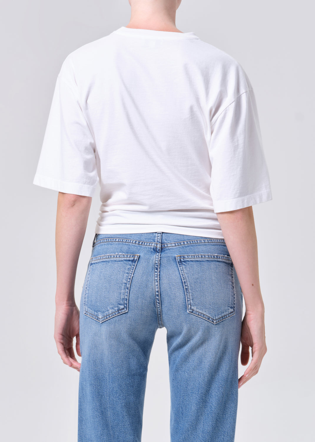 Person wearing a white t-shirt and light blue jeans on a plain background