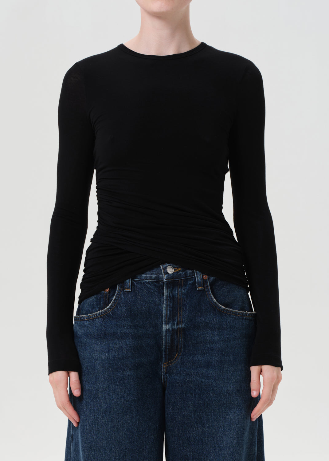 Person wearing a black long-sleeve top and blue jeans on a white background