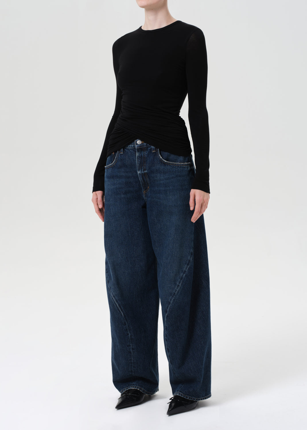 Person wearing a black long-sleeve top and blue jeans on a white background