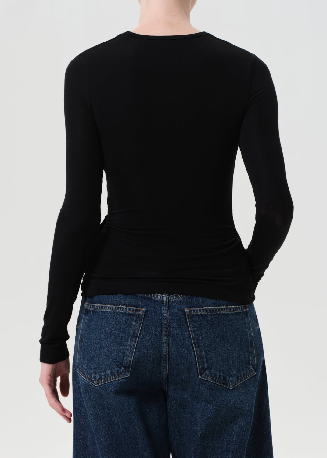 Person wearing a black long-sleeve top and blue jeans on a white background