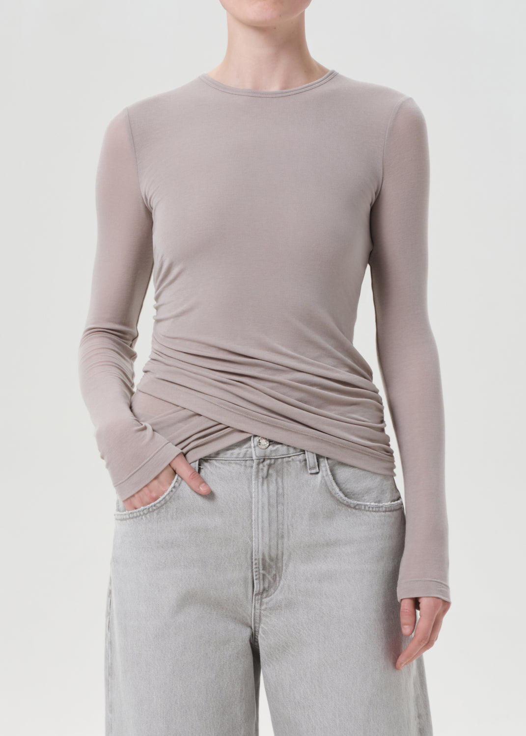 Person wearing a long-sleeve, fitted, light brown top with a plain background