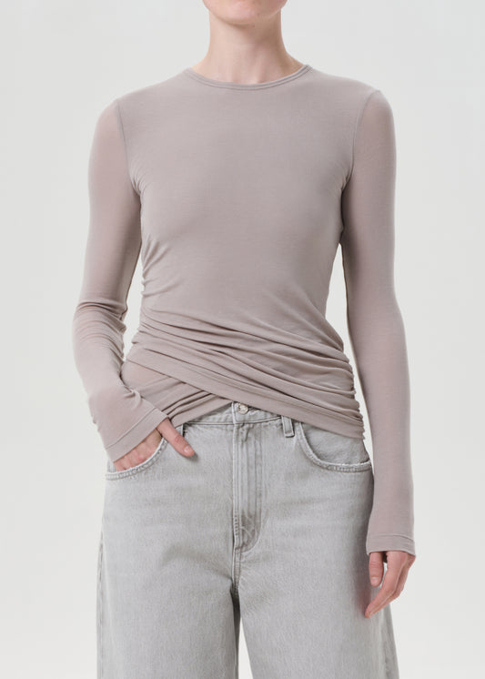 Person wearing a long-sleeve, fitted, light brown top with a plain background
