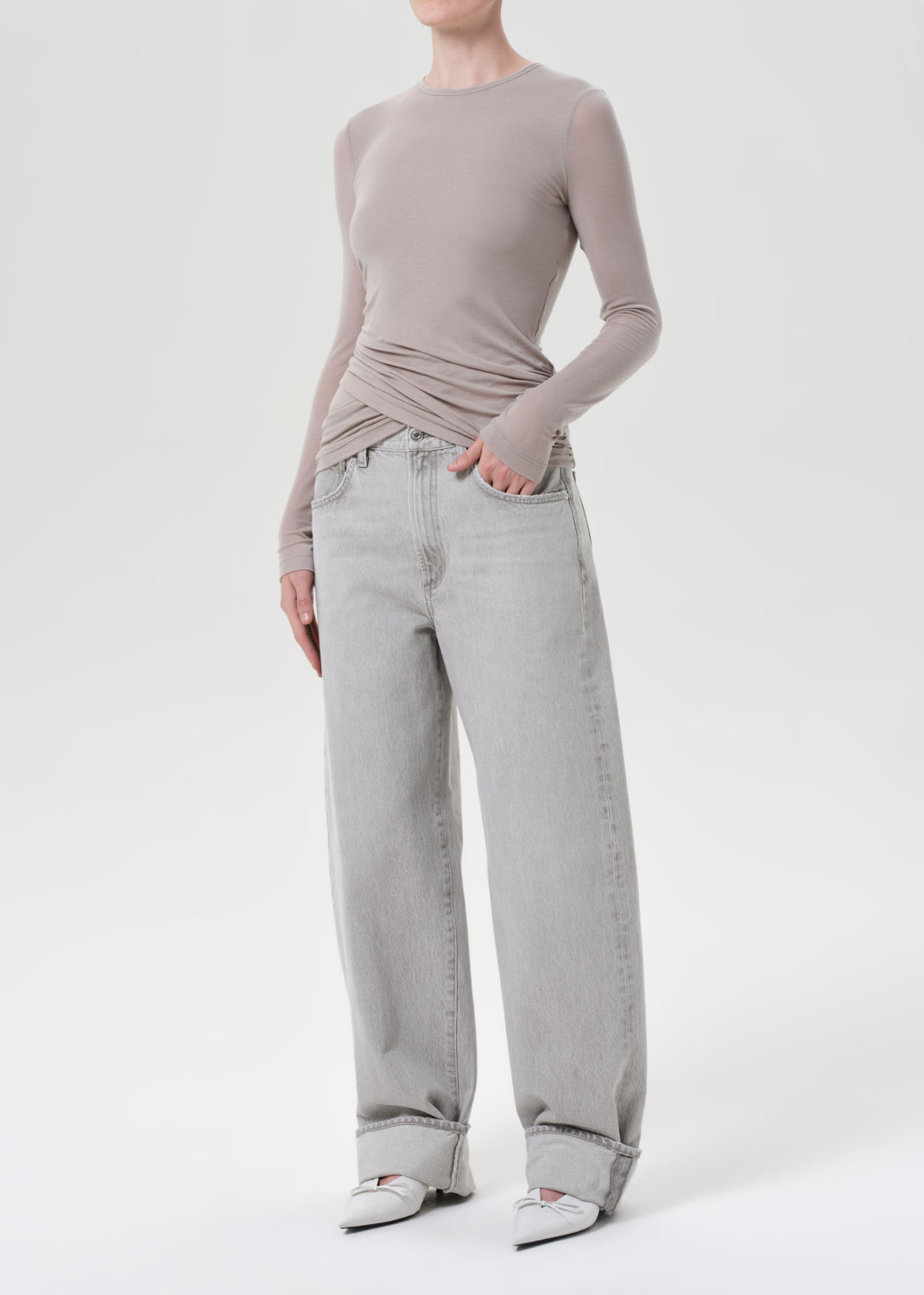 Person wearing a light gray long-sleeve top and light blue jeans on a white background