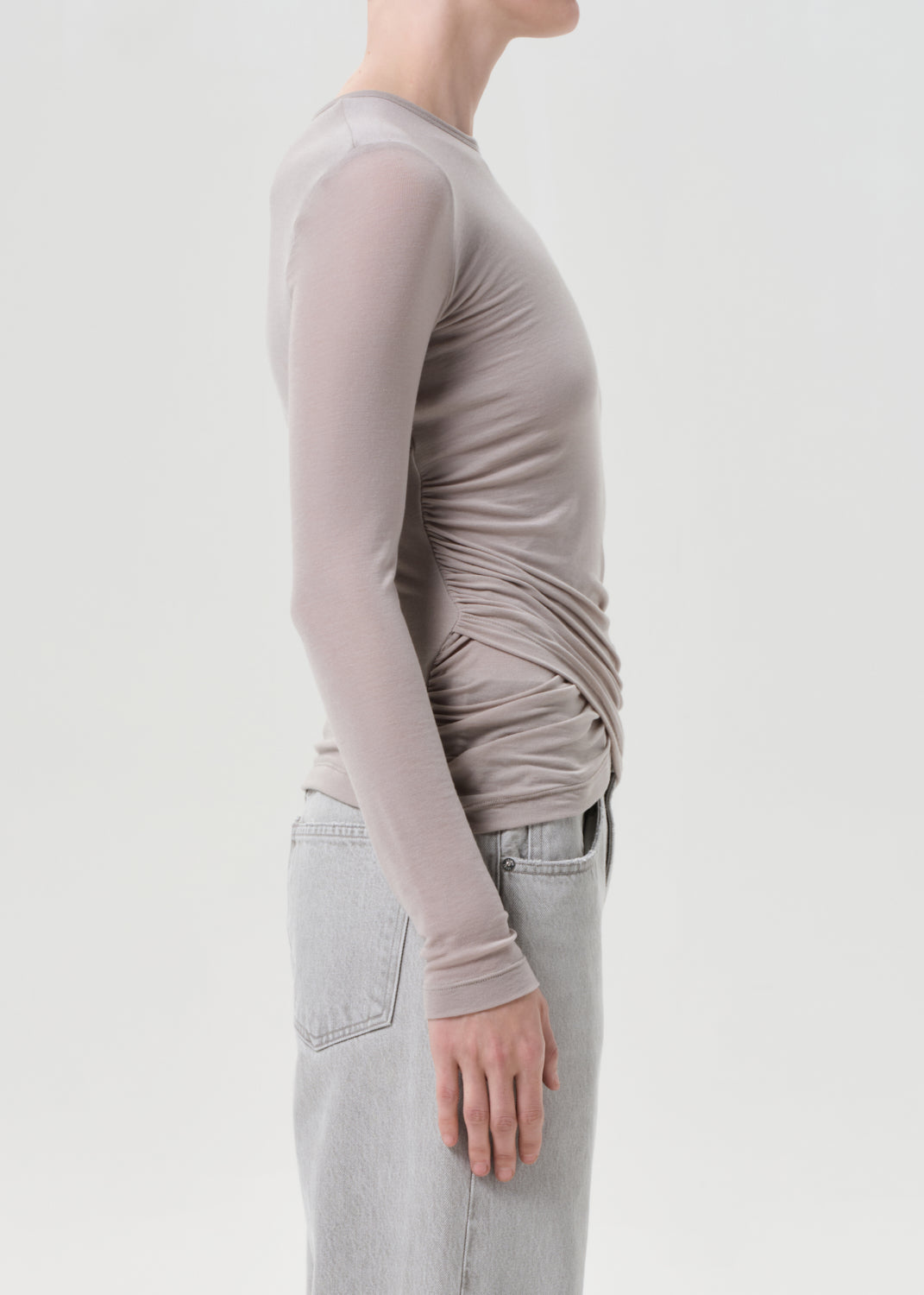 Person wearing a long-sleeve, light brown top and light gray pants on a plain background