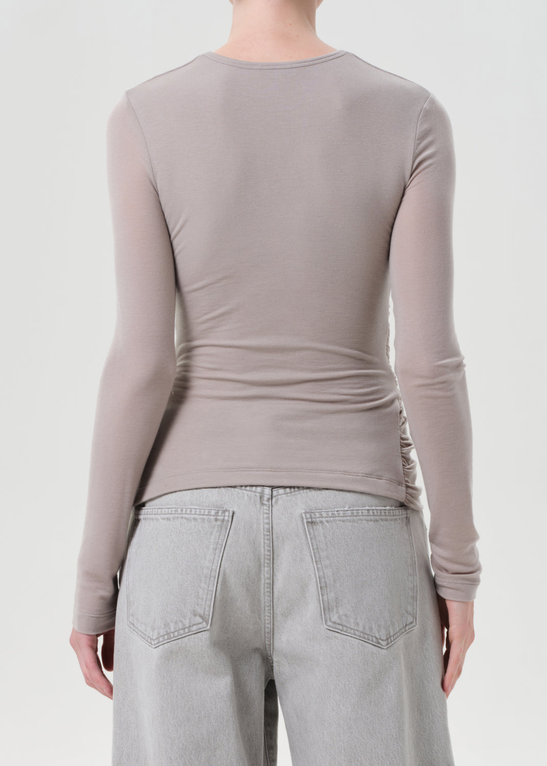 Person wearing a long-sleeve beige top and light gray pants on a white background