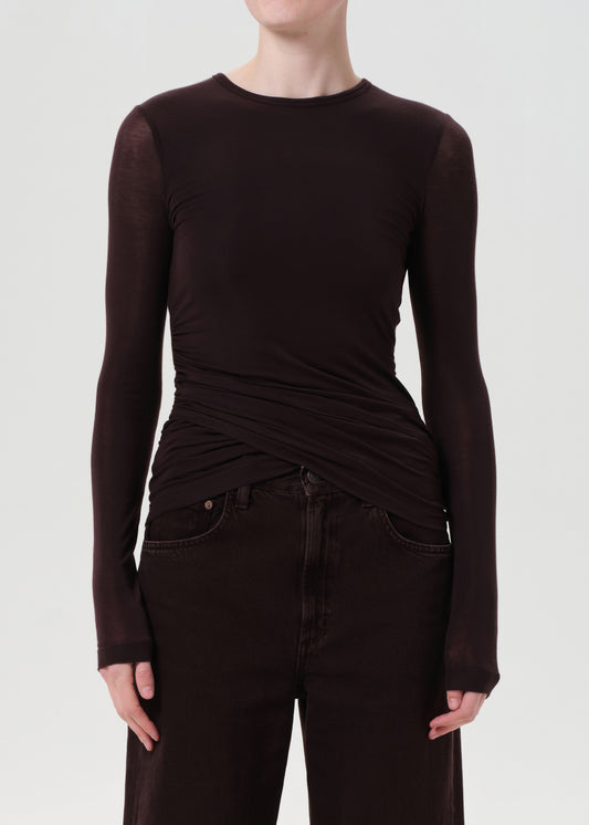 Person wearing a brown long-sleeve top and dark jeans on a white background