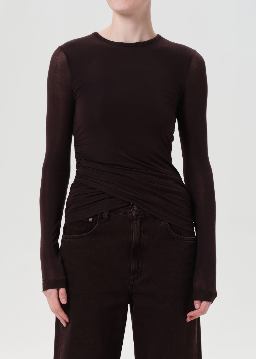 Person wearing a brown long-sleeve top and dark jeans on a white background