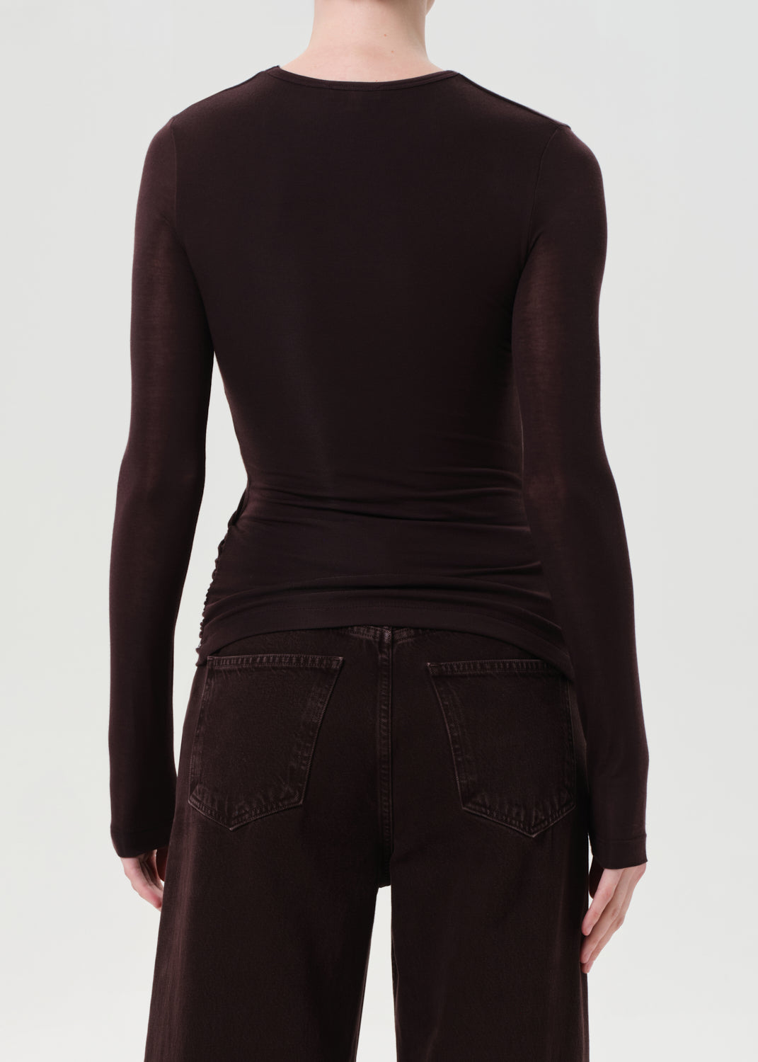 Person wearing a dark brown long-sleeve top and dark jeans on a white background