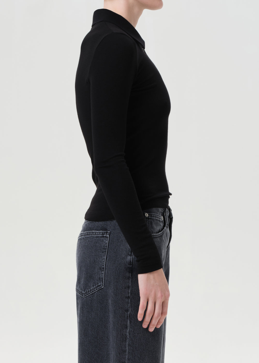 Person wearing a black long-sleeve top and dark jeans on a light gray background