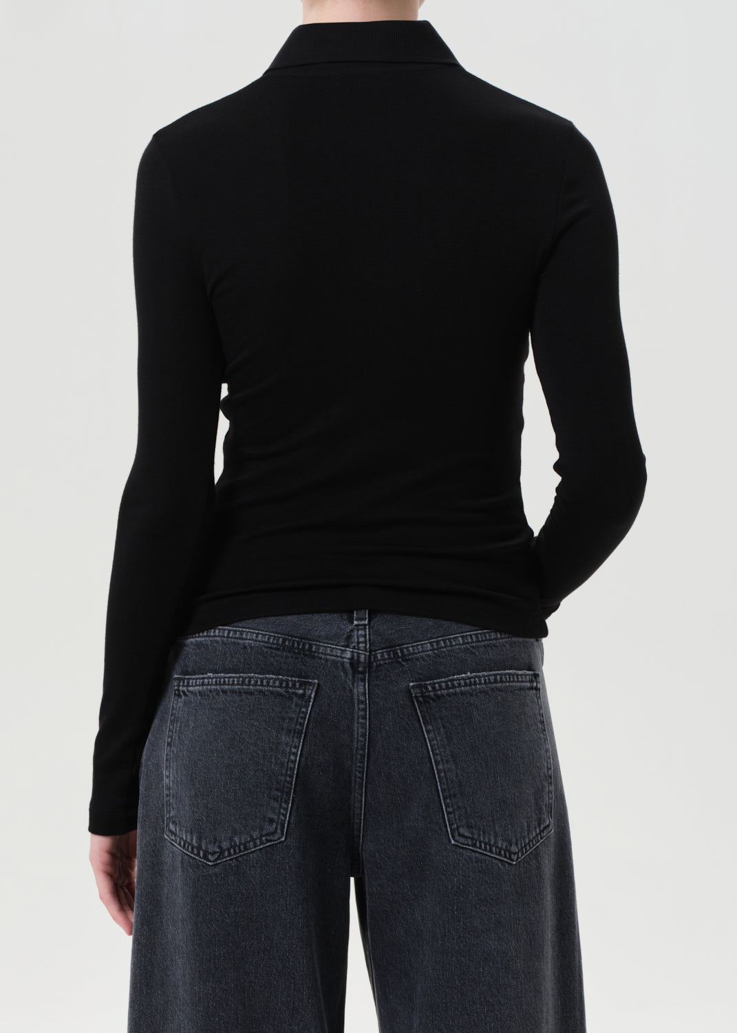 Person wearing a black long-sleeve top and dark jeans on a white background