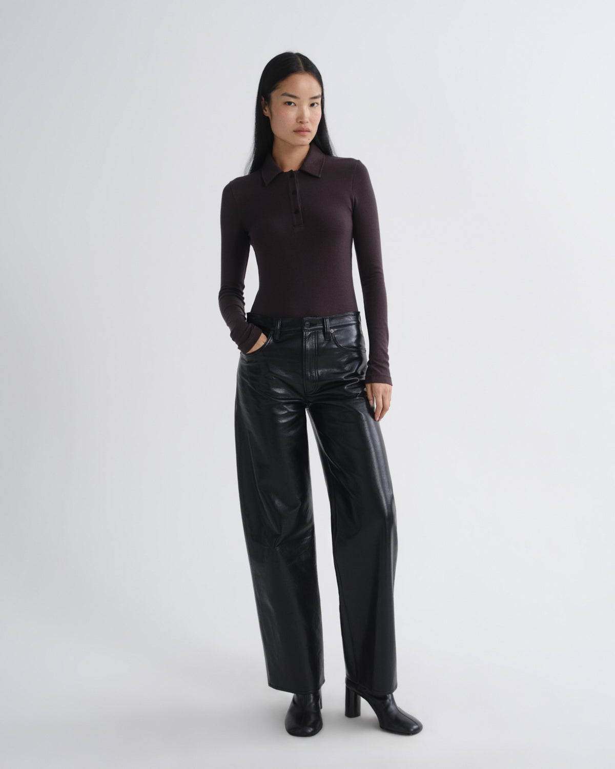 Person wearing a brown long-sleeve top and black leather pants on a white background