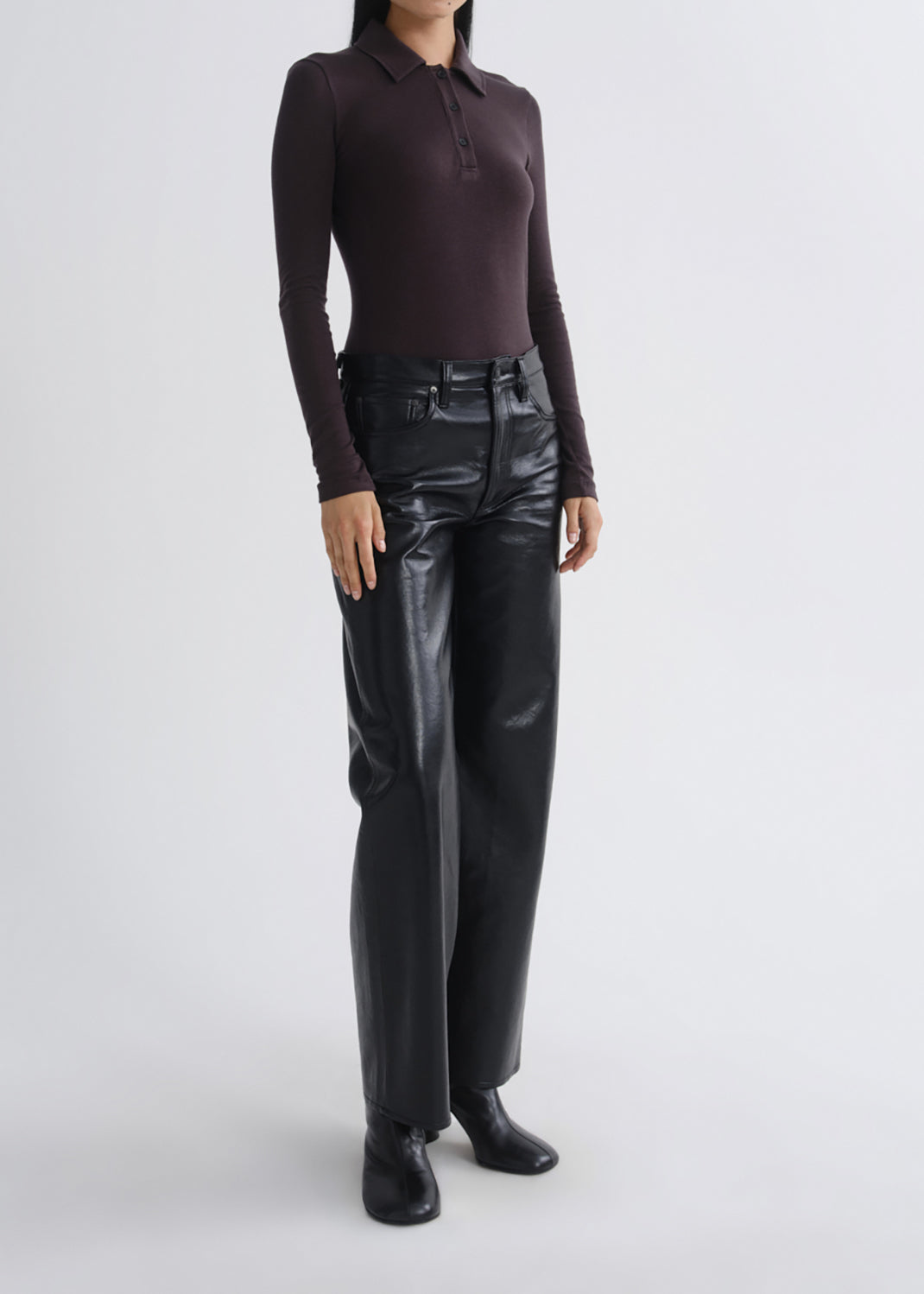 A model wearing a dark plum long-sleeve polo shirt and shiny black wide-leg trousers, standing against a grey background.