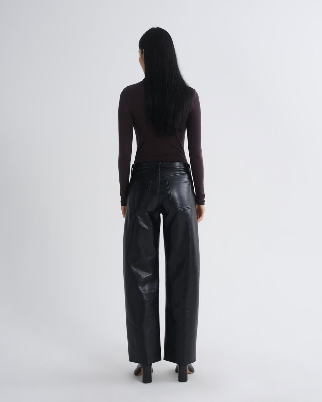 Person wearing black leather pants and a dark top on a white background