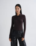 A woman modeling a dark plum long-sleeve polo shirt paired with black leather pants, shot against a plain light gray studio background.