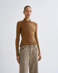 Woman wearing a brown long-sleeve polo shirt and beige pants on a grey background