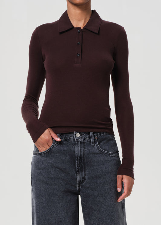 Person wearing a brown long-sleeve polo shirt and dark jeans on a light gray background
