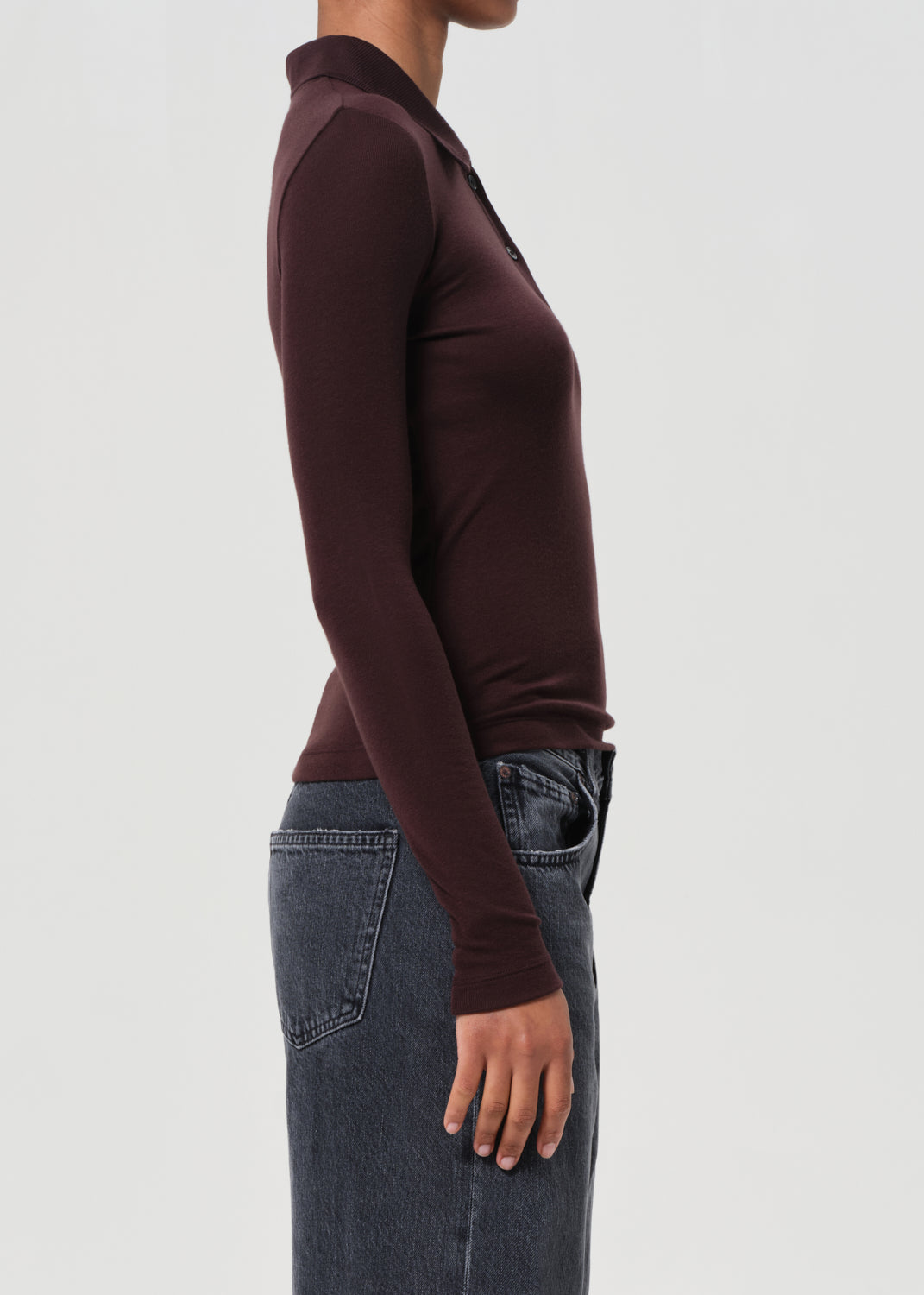 Person wearing a brown long-sleeve top and jeans on a light gray background