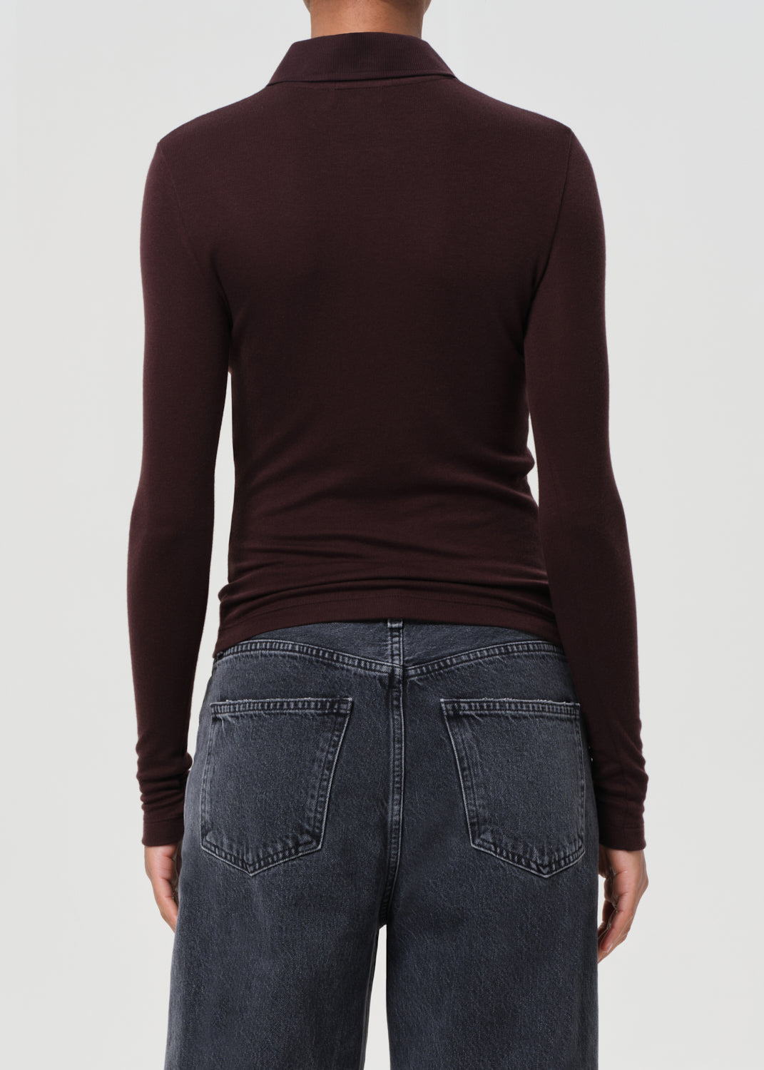 Person wearing a brown turtleneck and dark jeans on a white background